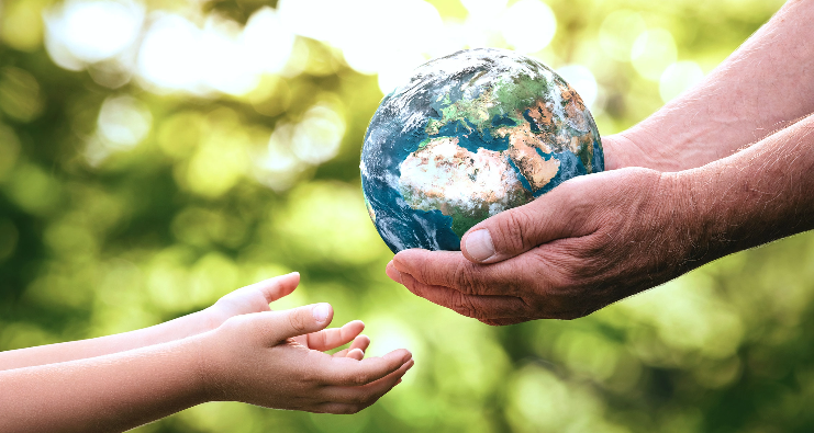 Manos de una persona mayor y un niño pasándose una bola del mundo en representación en el cooperativismo